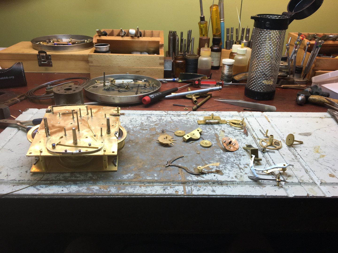 Clock movement parts and hand tools laid out flat on the workbench
