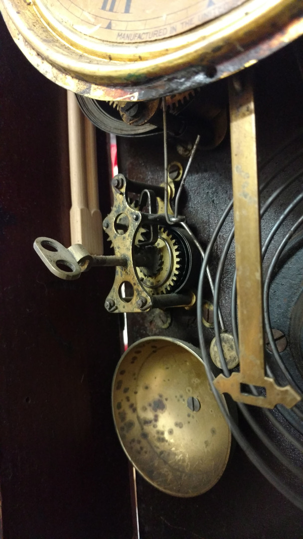 Inside an antique clock case — the winding key, strike work, coiled gong and brass bell seen behind the dial