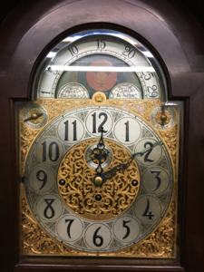 Close-up of an ornate grandfather clock dial with gilt filigree and a moon-phase arch