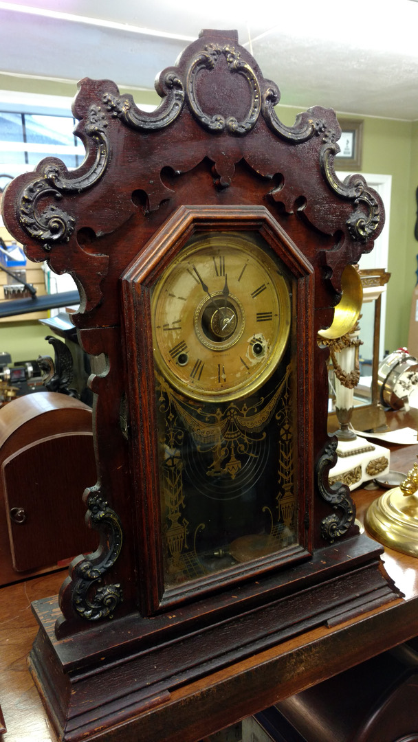 A restored dark-cased gingerbread parlor clock with pressed carving and painted glass