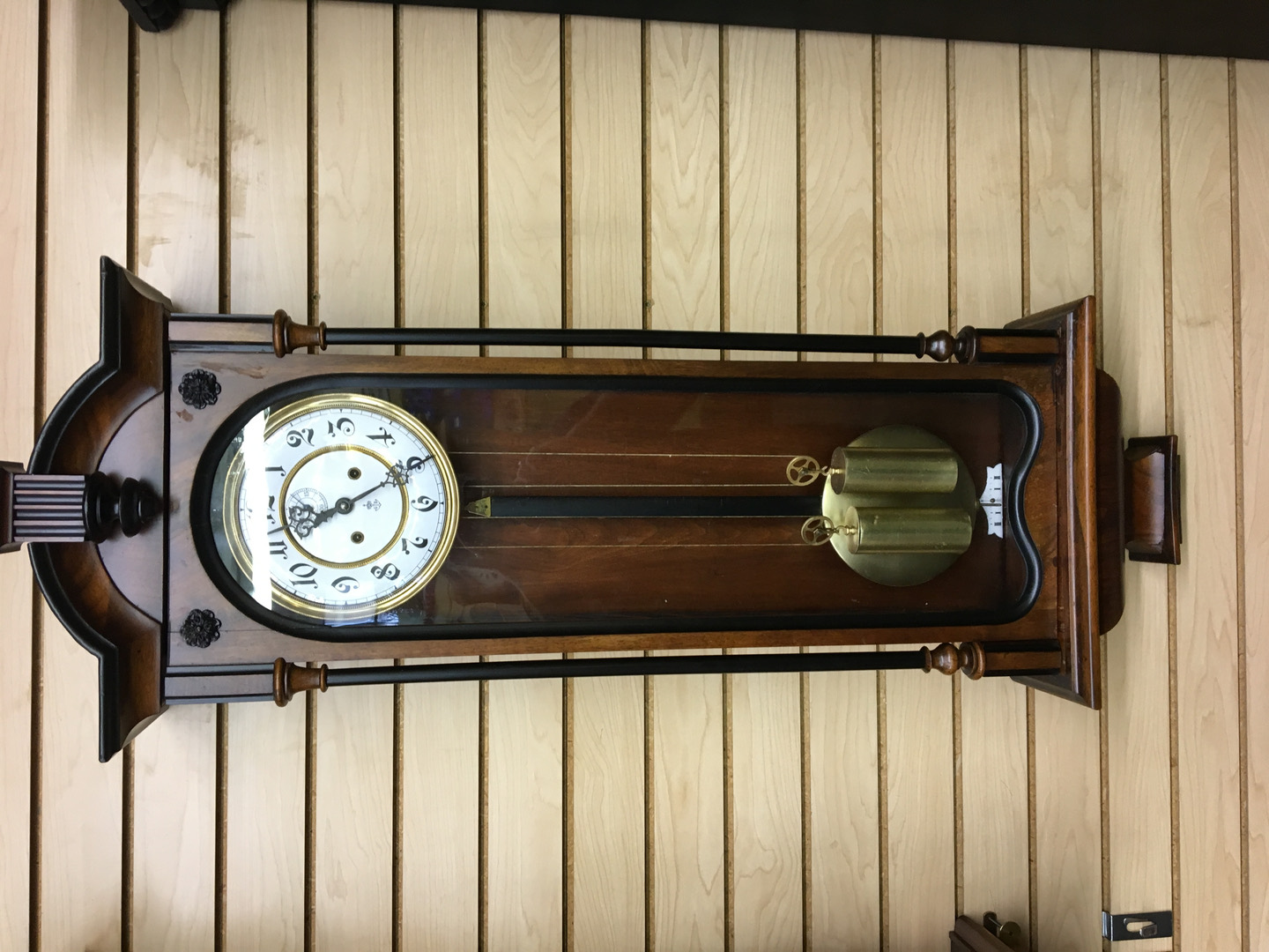 A restored walnut Vienna regulator wall clock with twin brass weights, hanging in the shop